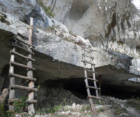 Foto de Antigua cueva excavada en la roca utilizada en la prehistoria por los hombres primitivos como refugio y reproducción de dos escaleras de madera - Imagen libre de derechos