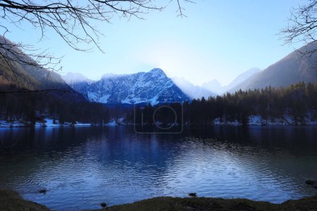 Picos montañosos nevados de los Alpes italianos en invierno y lago glacial sin gente en contraluz al atardecer