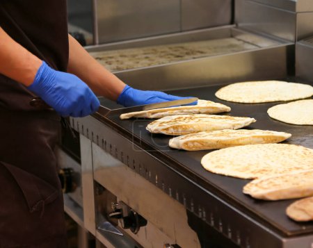 Foto de Experto chef con guantes de látex azul cocina piadina en la placa de metal caliente - Imagen libre de derechos