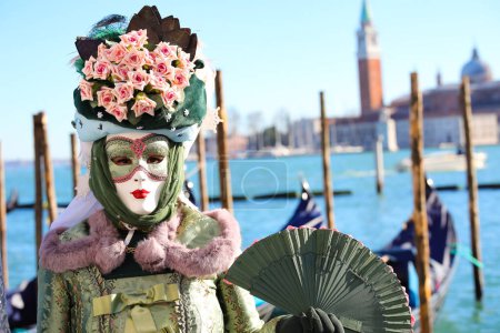 Téléchargez les photos : Venise, VE, Italie - 13 février 2024 : Femme masquée avec une élégante robe verte et un clocher Saint George en arrière-plan - en image libre de droit