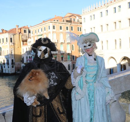 Téléchargez les photos : Venise, VE, Italie - 13 février 2024 : couple de personnes masquées et un petit chien sur le pont du rialto pendant le carnaval - en image libre de droit