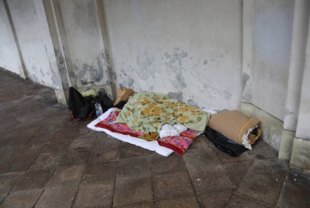 Téléchargez les photos : Le long de la route avec la couverture et un sans-abri dormant en dessous dans un état de pauvreté absolue - en image libre de droit