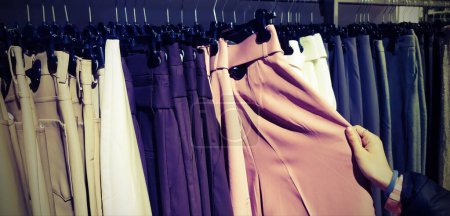 hand of young girl choosing trousers in trendy clothes shop with old toned effect
