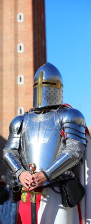 Photo for Medieval knight with steel armor and helmet to protect his head and old palace in background - Royalty Free Image