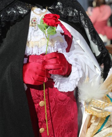 elegant lover with red rose flower in hand and ceremonial dress awaits his woman during the masquerade ball