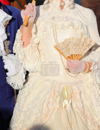 Edelfrau mit luxuriösem historischen Elfenbeinkleid und einem Fächer in der behandschuhten Hand während einer Party in Venedig Italien