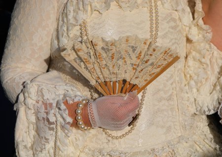 Edelfrau mit luxuriösem elfenbeinweißem historischen Kleid und einem Fächer in der behandschuhten Hand bei der Maskerade-Karnevalsparty in Venedig