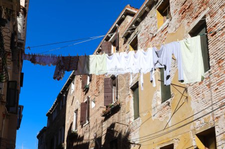 Téléchargez les photos : Nombreux vêtements suspendus et linge séchant au soleil dans l'allée étroite entre les maisons - en image libre de droit