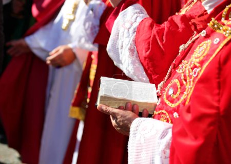 Älterer Bischof mit roter Soutane und Bibel in der Hand während des religiösen Ritus im Gotteshaus