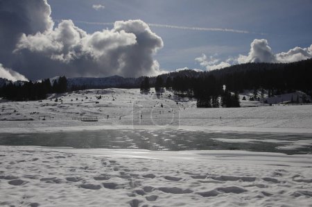frozen mountain lake in winter with white snow and white clouds in backlight