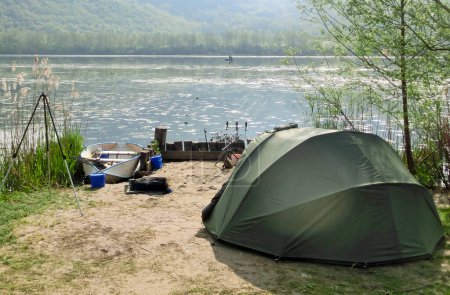 Téléchargez les photos : Tente verte de pêcheurs sur la rive du lac attendant d'attraper des poissons avec leur matériel de pêche - en image libre de droit