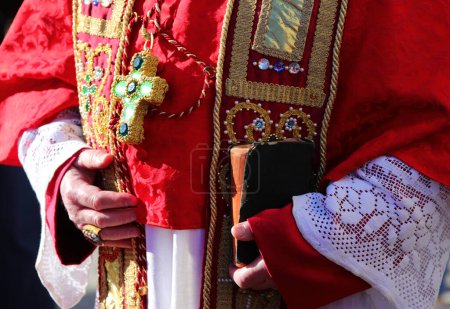 priest with red robe holding bible in hand during religious ceremony in church