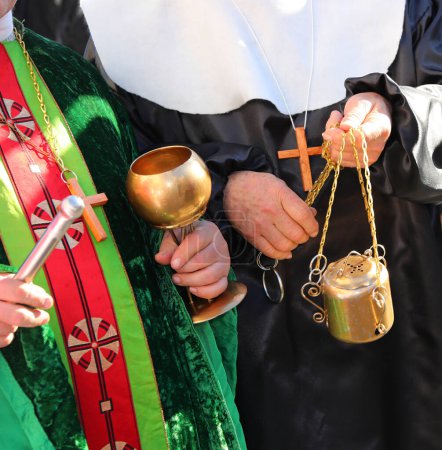 Senior priest with cassock and aspergillum while performing the blessing also with holy water and incense during the holy mass