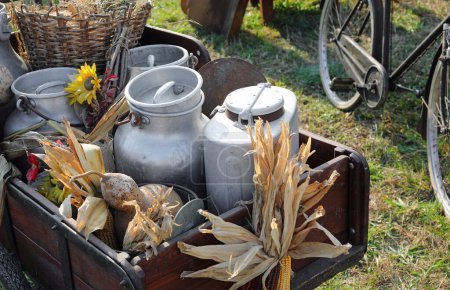 collection de boîtes de lait altérées en aluminium débordant de produits frais de la ferme, nichées dans un chariot en bois à l'ancienne évoquant un sentiment de nostalgie pour des temps plus simples
