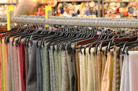 Téléchargez les photos : Vêtements tissus et pantalons soigneusement disposés sur un porte-vêtements dans un magasin. Les vêtements sont organisés par couleur et par type, et le rack est bien éclairé. - en image libre de droit