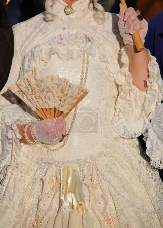 Edelfrau mit luxuriösem elfenbeinweißem historischen Kleid und einem Fächer in der behandschuhten Hand bei einer Maskenparty in Venedig