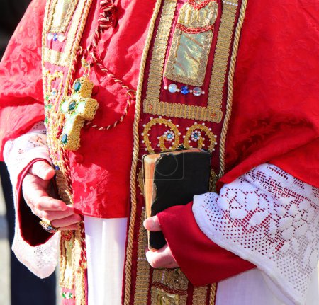 Foto de Biblia con los escritos sagrados en las manos del obispo durante el rito religioso con vestimenta clerical roja - Imagen libre de derechos