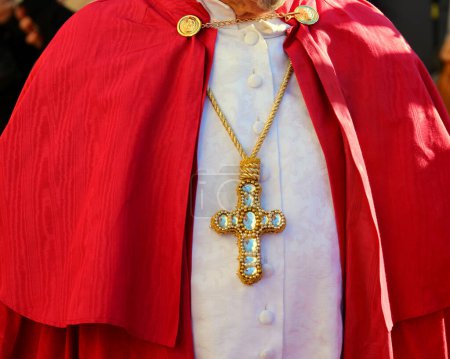 Priest in a ceremonious red cassock and a large jeweled cross blessing at Mass