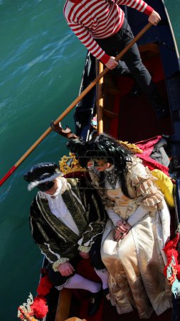 Photo for Masked honeymoon couple on gondola in venice during carnival and gondolier - Royalty Free Image