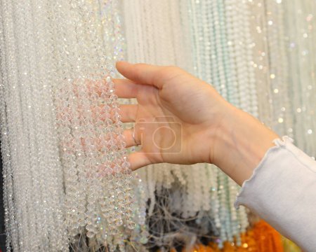 Hand eines jungen Mädchens inmitten weißer Kristallketten in einem Juweliergeschäft