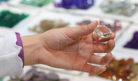 Téléchargez les photos : Main d'une fille tenant une pierre très précieuse qui ressemble à un diamant ou un zircon à vendre dans la boutique de gemmes - en image libre de droit