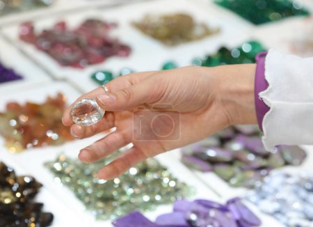 Téléchargez les photos : Main d'une jeune fille tenant une pierre très précieuse qui ressemble à un diamant ou un zircon à vendre dans la boutique de gemmes - en image libre de droit