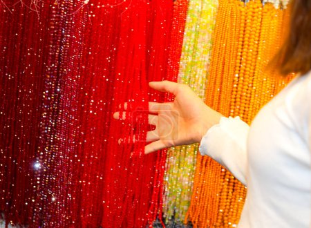 main d'une jeune femme alors qu'elle choisit un collier de perles en verre rouge dans la bijouterie fantaisie du centre commercial