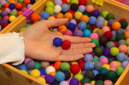 mano de una niña con dos bolas rojas y azules de lana que simbolizan el género femenino y masculino