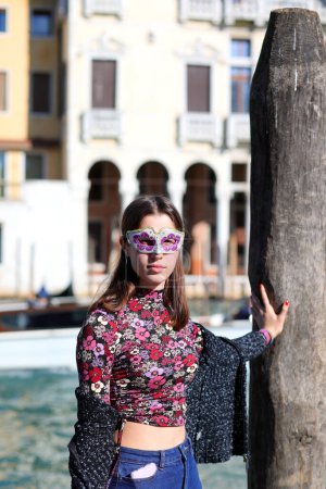 Téléchargez les photos : Jeune fille avec masque vénitien posant à Venise sur la rive du Grand Canal à Venise - en image libre de droit