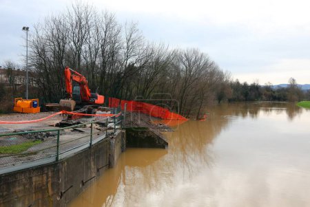 red excavator on the embankment of the river in flood during the flood in a road construction site for the maintenance of the riverbed