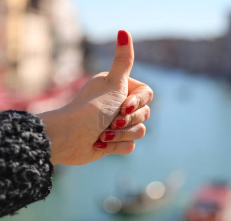 Thumb up ok sign of hand of young Girl with nails with red nail polish and grand canal in venice in ITALY