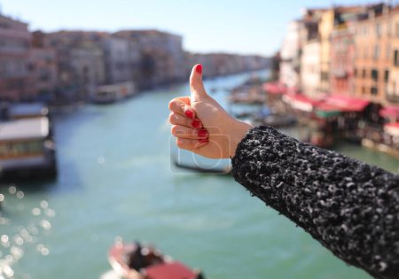 Thumb up ok sign of hand of young gilr with nails with red nail polish and grand canal in venice in ITALY