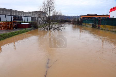 Überflutung des Flusses im Industriegebiet der Stadt mit Lagerhallen und Fabrik aufgrund des Klimawandels