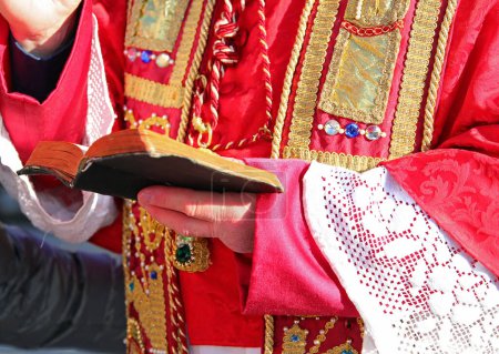 Religious Pastor in Red Vestments Blessing with Bible in Hand