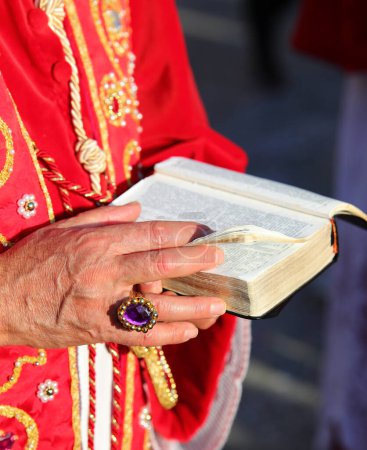 Hand of elderly priest wearing large ring holding Bible during Eucharistic celebration