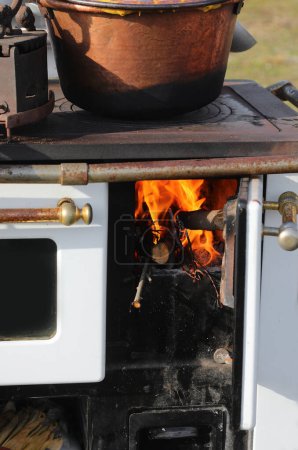 Holzofen in einer Küche mit eingeschaltetem Feuer und einem Kupfertopf darauf, um Polenta zuzubereiten, eine typisch norditalienische Speise aus gelbem Maismehl.