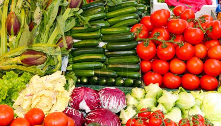 Vibrant display of fresh fruits and vegetables including artichokes zucchini and tomatoes at a farmers market stall.