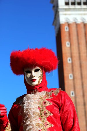 Photo for Venice, VE, Italy - February 13, 2024: Masked person with red hat and Famous Bell tower of Venice and sky in background - Royalty Free Image