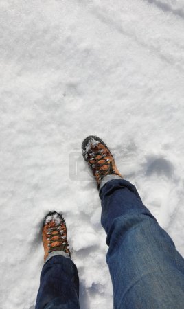 Mountain boots with legs of young hiker during trip on high white soft snow in winter