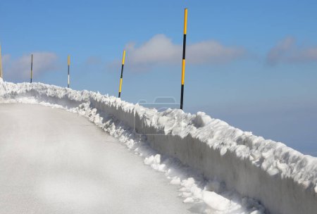 poteaux peints en jaune et noir coincés dans la neige pour délimiter le bord de la route de montagne glacée en hiver