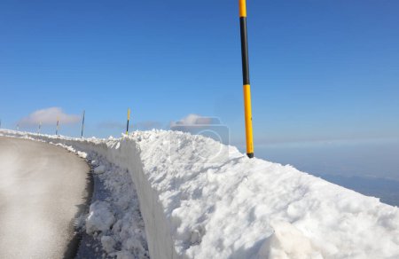 yellow-and-black snow poles mark the edge of an icy mountain road in winter