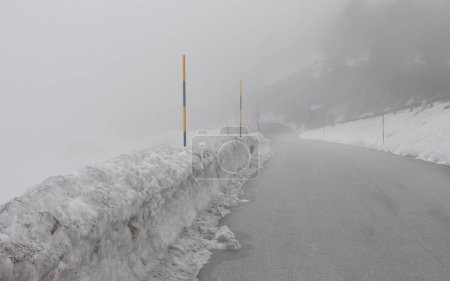 Eisige Bergstraße mit schlechter Sicht durch dichten Nebel und Schnee an den Rändern