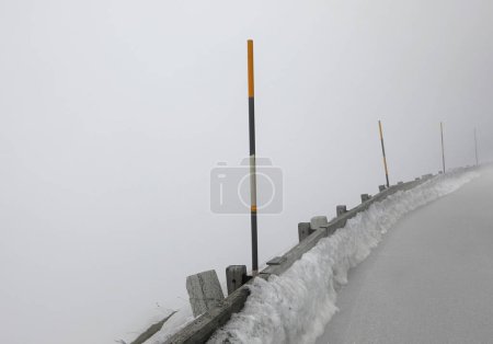Eisige Bergstraße mit schlechter Sicht durch dichten Nebel und Schnee