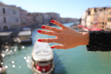 Téléchargez les photos : Main de jeune femme aux doigts élancés et aux ongles roux et Grand Canal de Venise avec des bateaux - en image libre de droit