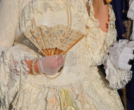 Primer plano de la mano guante sosteniendo ventilador de dama noble en prendas de vestir antiguas y lujosas