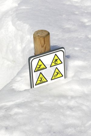 La neige fraîche enterre un panneau d'avertissement avec des pictogrammes avertissant du danger de chute et de glissement dû à la glace