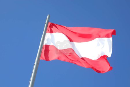 Österreichische Flagge in weiß-roten Farben weht vor blauem Himmel