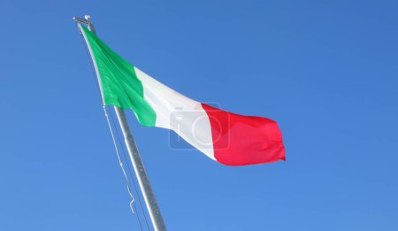 Large Italian flag with green white and red colors waving in the cloudless blue sky