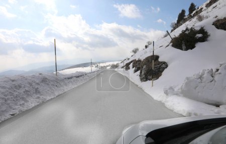 icy mountain road with snow on the sides and posts to mark the limit of the roadway seen from inside a car