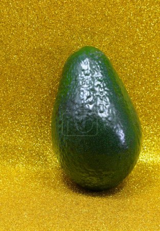 grüne Avocadofrucht mit Schale ideal als gesundes Ernährungs- und Wellness-Konzept auf goldenem Hintergrund